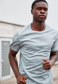 Lysegrå atletisk T-shirt lavet af åndbart stof, med rund halsudskæring og korte ærmer; enkelt design med diskret branding.