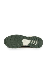 Semelle de basket présentant un design en caoutchouc vert, surface texturée, motifs circulaires et hexagonaux pour l'adhérence, et un accent de logo beige.