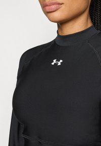 Μαύρο αθλητικό μπλουζάκι μακρυμάνικο με ψηλό γιακά. Διαθέτει εφαρμοστή γραμμή, λεία υφή και λευκό λογότυπο Under Armour στο στήθος.