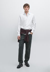 White button-up shirt, dark green trousers, maroon sweater tied around the waist, and black leather shoes. Simple, modern design.