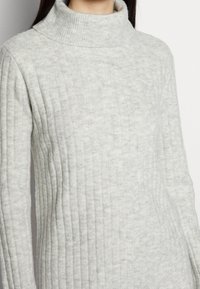 Maglione a coste grigio chiaro con un design a collo alto, caratterizzato da una texture morbida e una silhouette aderente, che enfatizza i pattern verticali.