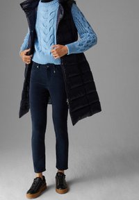 Marinblå pufferväst över en ljusblå kabelstickad tröja, mörka jeans och svarta sneakers med plattformssula. Texturerade stickdetaljer synliga.