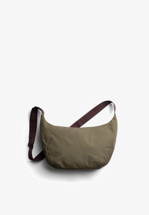 Sac bandoulière vert olive avec une finition douce et texturée, doté d'une sangle bordeaux et d'un petit logo sur le devant. Forme arrondie, design minimaliste.