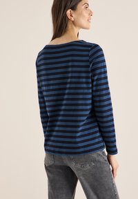 Mørkeblå langærmet skjorte med vandrette mørkeblå striber, der har en bred halsudskæring og en afslappet pasform, parret med grå jeans.