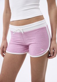 Shorts de sport rayés roses avec une taille élastique blanche et un cordon de serrage. Présente un bord blanc le long de l'ourlet et un petit logo sur le côté.