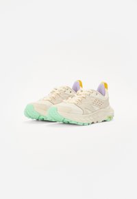 Helle beige Sportschuhe mit einem strukturierten Obermaterial, mintgrüner Sohle und Akzenten in Lila und Gelb. Mit runden Schnürsenkeln und seitlichen Perforationen.