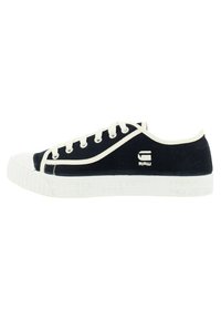 Zapatillas de lona de color marino con puntera de goma blanca y suela texturizada, que cuentan con cordones blancos y logotipo en el costado. Forma redondeada con un diseño de bajo perfil.