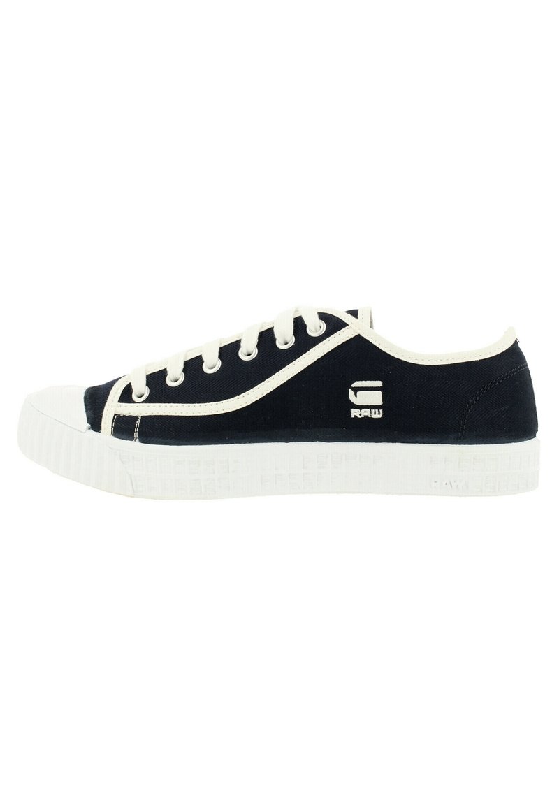 Zapatillas de lona de color marino con puntera de goma blanca y suela texturizada, que cuentan con cordones blancos y logotipo en el costado. Forma redondeada con un diseño de bajo perfil.