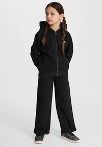 Czarna bluza z suwakiem i kapturem, w zestawie z pasującymi czarnymi dresami. Posiada małe logo na piersi i nogawce spodni.