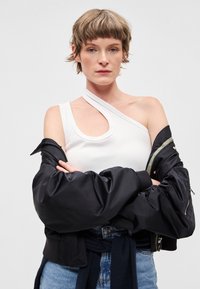 Ασύμμετρη λευκή κορυφή τύπου tank με λαιμόκοψη με κοψίματα, συνδυασμένη με μαύρο bomber μπουφάν, που διαθέτει ριμπ τελείωμα και διακοσμητικά φερμουάρ.