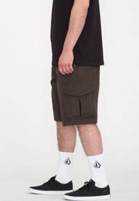 Olivengrønne cargo shorts med sidelommer, designet med en løs pasform. Båret med hvide sokker med logo og sorte sneakers.