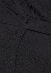 Tecido preto texturizado com uma aparência ligeiramente enrugada, apresentando um design entrelaçado suave e detalhes de costura subtis.