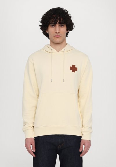 Cream-colored hoodie with a front kangaroo pocket, drawstring hood, and a brown cross logo on the chest. Soft texture, casual fit.