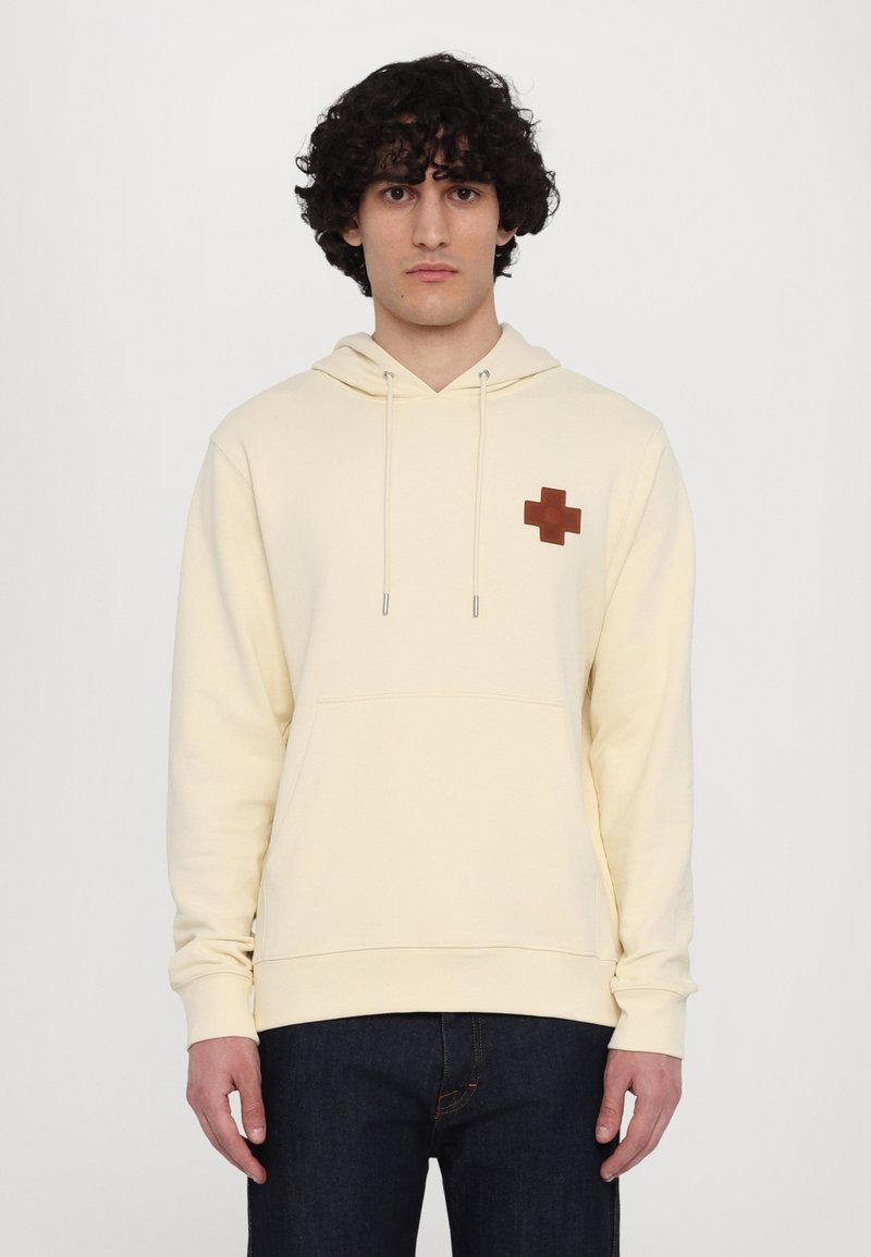 Cream-colored hoodie with a front kangaroo pocket, drawstring hood, and a brown cross logo on the chest. Soft texture, casual fit.