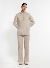 Beżowy sweter z prążkowanej dzianiny z kieszenią z przodu, w połączeniu z pasującymi spodniami z prążkowanej dzianiny. Luźny krój, długie rękawy i kaptur ze sznurkiem.