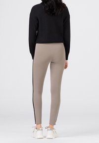 Leggings beige con strisce nere ai lati, abbinati a un maglione nero a trama. I leggings hanno una vestibilità slim e sono lunghi fino alla caviglia.
