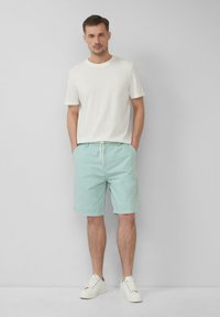 Hellgrau, kurzärmeliges T-Shirt kombiniert mit hellmintgrünen Shorts mit Kordelzug. Das Modell trägt weiße Sneakers. Einfaches, lässiges Design.
