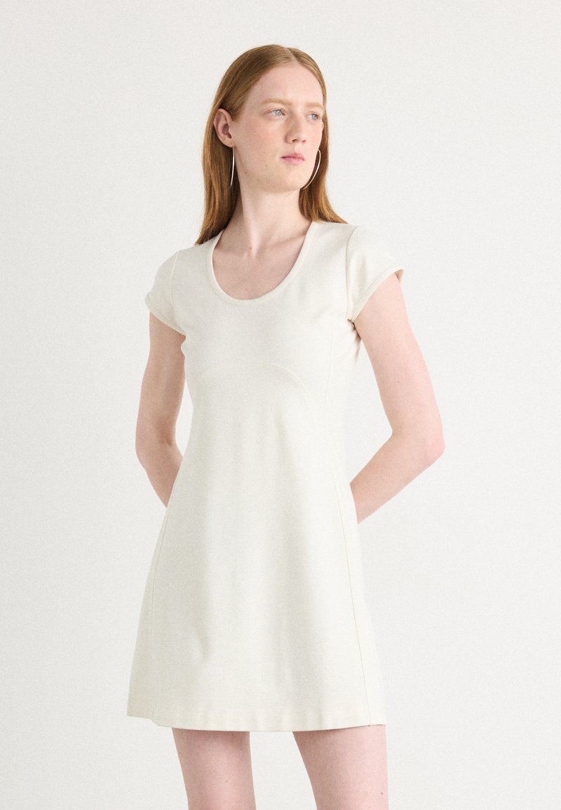 Cap mouw, lichtbeige jurk met een ronde hals. Glad materiaal met subtiele naden, uitlopende rok die tot halverwege de dij komt. Eenvoudig en minimalistisch ontwerp.