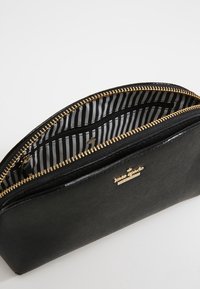 Černá zipová taštička z texturovaného materiálu, s pozlaceným zipem a pruhovanou podšívkou, obsahující malou zipovou kapsu a detail s logem.
