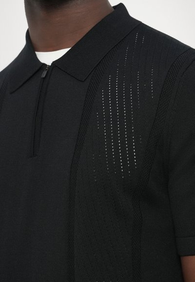 Polo preta com tecido texturizado e perfurações verticais de um lado, mangas curtas e gola com fecho de correr.