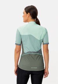 Maillot de cyclisme léger en tons de vert avec des manches courtes, ajusté près du corps et des accents en maille. Il présente des motifs color-block courbés et un logo à l'arrière.