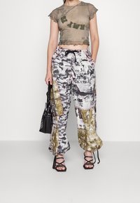 Przezroczysty, oliwkowozielony top z falbaniastym dołem, w zestawie z luźnymi, wzorzystymi spodniami w kolorze czarnym, białym i złotym. Czarna torebka, sandały na obcasie.