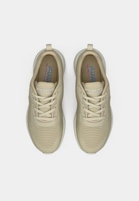 Beige sportcipők texturált felsőrésszel, kerek orral és gumitalppal. Jellemzők közé tartozik az egy színű fűző és a nyelvén található logó.