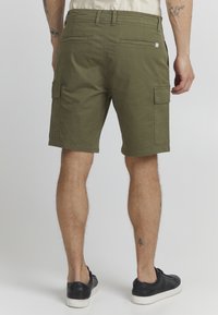 Shorts cargo verts olive avec poches avant et arrière, passants de ceinture et coupe décontractée. Fabriqués en tissu coton, offrant une texture légère.