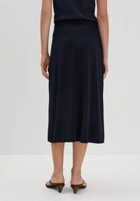 Jupe midi marine en tissu doux, dotée d'un design évasé et d'une taille élastique. Portée avec des sandales à talons brunes.