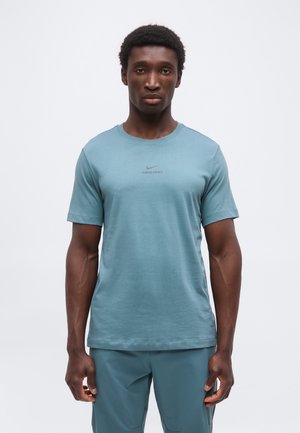 Mężczyzna w jasno niebieskiej sportowej koszulce Nike Pro z krótkim rękawem i dopasowanych szortach, stojący na jednolitym białym tle.