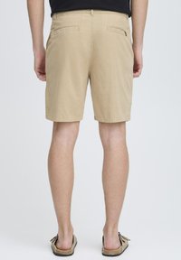 Shorts khaki en tissu léger, avec deux poches arrière et une coupe droite, arrivant juste au-dessus des genoux.
