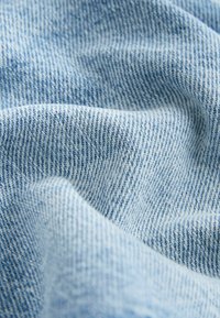 Gaiši zila džinsa audums ar smalku tekstūru, kas izveidots ar tīkla aušanas tehniku un redzamu šuvi tumšākā zilā krāsā, radot izteiktu rakstu.