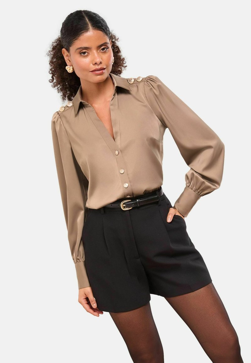Silk blouse in taupe with a V-neck, button-up front, and puffed sleeves, paired with black tailored shorts and a thin belt, showcasing gold hardware.