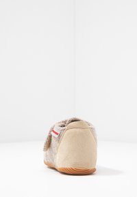 Szare-brązowe tekstylne kapcie o miękkiej, puszystej fakturze; mają beżowy zamszowy obcas i gumową podeszwę; zawierają czerwoną metkę z boku.