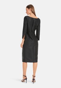 Schwarzes, knielanges Kleid mit dreiviertel Ärmeln und leichtem Glanz. Verfügt über einen Rundrücken und einen verdeckten Reißverschluss. Dezente seitliche Schlitze.