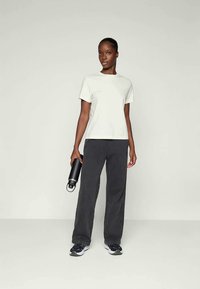 Ανοιχτό γκρι κοντομάνικο μπλουζάκι συνδυασμένο με σκούρο γκρι παντελόνι φάρδους. Το μοντέλο κρατάει ένα μαύρο μπουκάλι νερού και φοράει μαύρα αθλητικά παπούτσια.