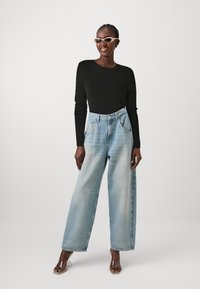 Zwarte lange mouwen top, lichtblauwe wijde jeans met vervaagde details, en doorzichtige haksandalen met bandjes. Soepele, losse pasvorm over het geheel.