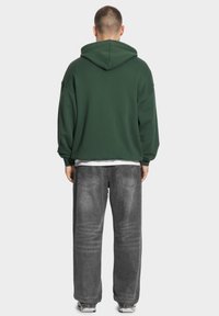 Zielona, oversize'owa bluza z teksturowanym wykończeniem, z kieszenią kangurką i regulowanym kapturem, w zestawie z wyblakłymi szarymi dżinsami.