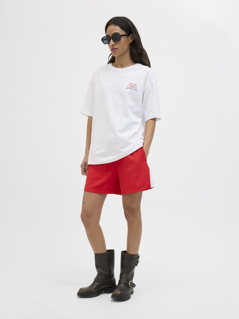 Witte oversized T-shirt met "Coffee" grafiek, gecombineerd met rode shorts en zwarte leren kniehoge laarzen. Soepele texturen, casual ontwerp.