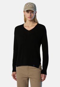 Schwarzer V-Ausschnitt-Pullover aus weichem Material mit geripptem Saum und Bündchen, kombiniert mit einer beigen Cordmütze mit weiß gesticktem Text.