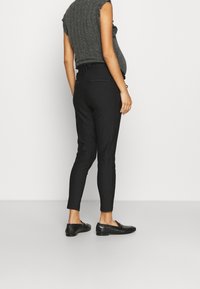 Pantalones negros a rayas con un corte ajustado, cinturilla elástica y diseño minimalista, combinados con zapatos negros planos.