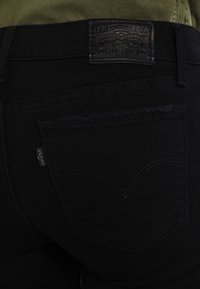 Los jeans de mezclilla negra cuentan con un bolsillo trasero con forma de corazón cosido y una etiqueta de cuero grabada con el logotipo de la marca. Presentan sutiles detalles desgastados.