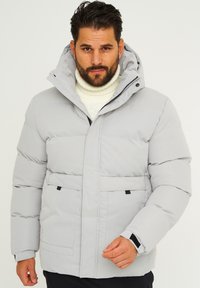 Hellgraue Steppjacke mit Kapuze, ausgestattet mit einem Frontreißverschluss, zwei unteren Taschen und elastischen Bündchen für zusätzliche Wärme. Strukturiertes Gewebe mit gestepptem Muster.