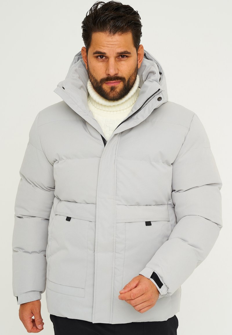 Hellgraue Steppjacke mit Kapuze, ausgestattet mit einem Frontreißverschluss, zwei unteren Taschen und elastischen Bündchen für zusätzliche Wärme. Strukturiertes Gewebe mit gestepptem Muster.