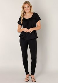 Zwart topje met korte mouwen en geplooide halslijn, gecombineerd met zwarte legging. Gladde textuur en aansluitend ontwerp. Gedragen met zwarte sandalen met bandjes.