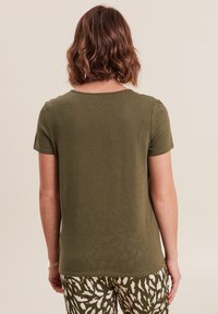 T-shirt verde oliva a maniche corte con scollatura rotonda, texture morbida e vestibilità rilassata. Abbinato a pantaloni con fantasia verde e bianca.