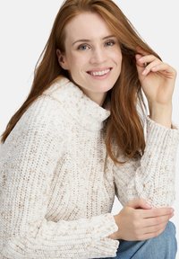 Chunky knit sweater in cream with beige flecks, featuring a high collar and ribbed cuffs. Soft texture and relaxed fit.