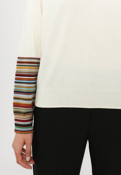 Maglione a maglia color crema con maniche a strisce multicolori. Texture morbida, vestibilità rilassata, fondo a contrasto nero. Linee pulite e design minimalista.