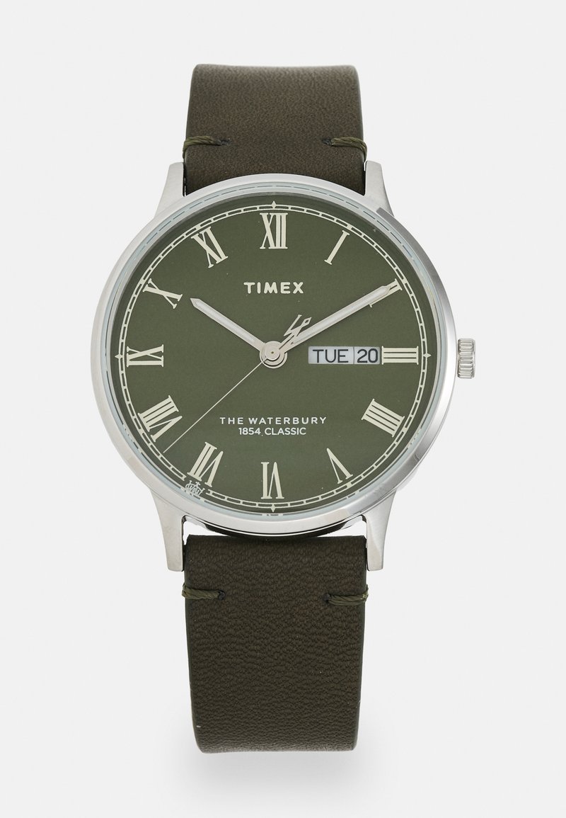 Montre Timex avec un cadran analogique vert, des chiffres romains, un boîtier argenté et un bracelet en cuir vert foncé. Affiche la date et le jour de la semaine.