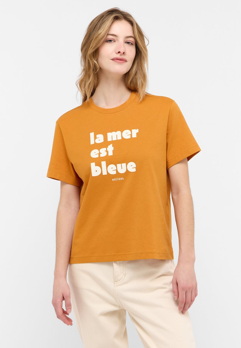 Trumpas rankovėmis oranžinis marškinėliai su baltu tekstu "la mer est bleue." Paprastas kirpimas, apvalios kaklo dizainas. Kombinuojama su šviesių spalvų kelnėmis.